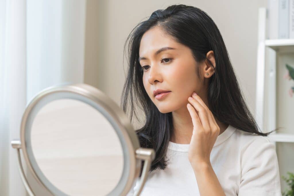 Woman looking at her face in the mirror examining for acne breakouts