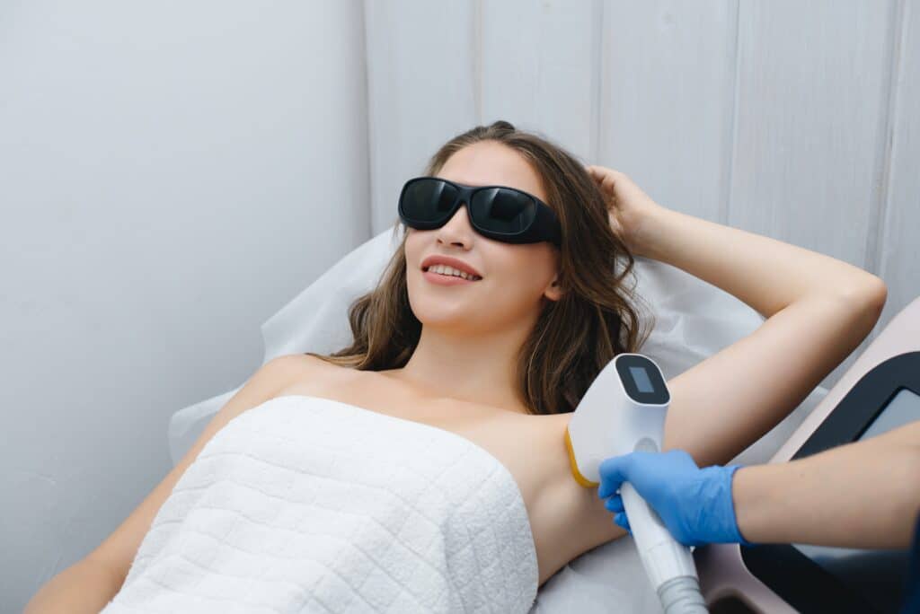 Woman, wearing dark sunglasses, smiles as her doctor administers laser hair removal treatment